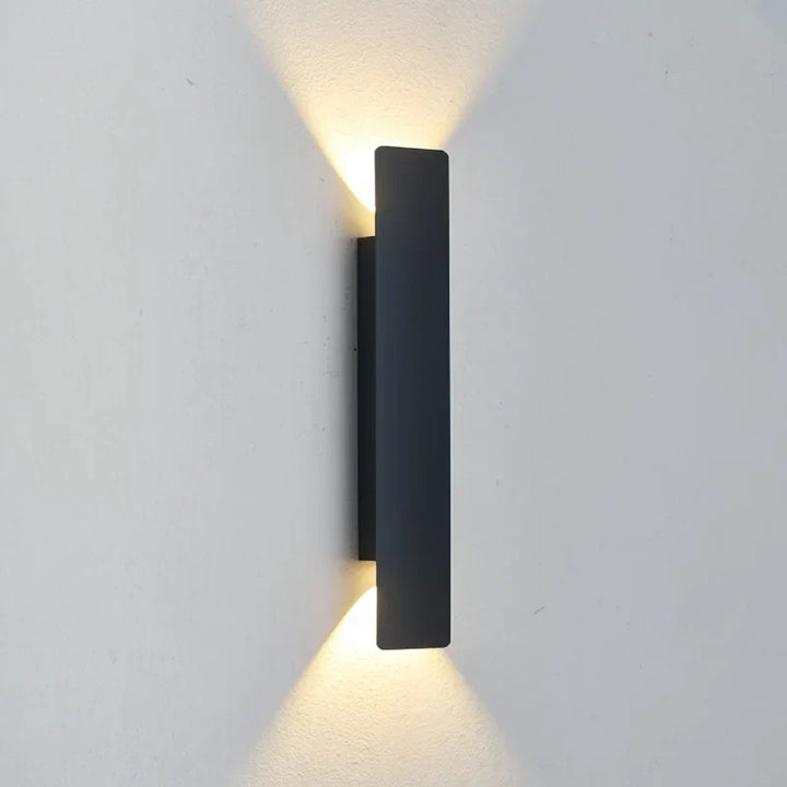 Applique noire rectangulaire allongée fixée sur un mur clair, vue de trois quarts, diffusant une lumière chaude en haut et en bas. 4