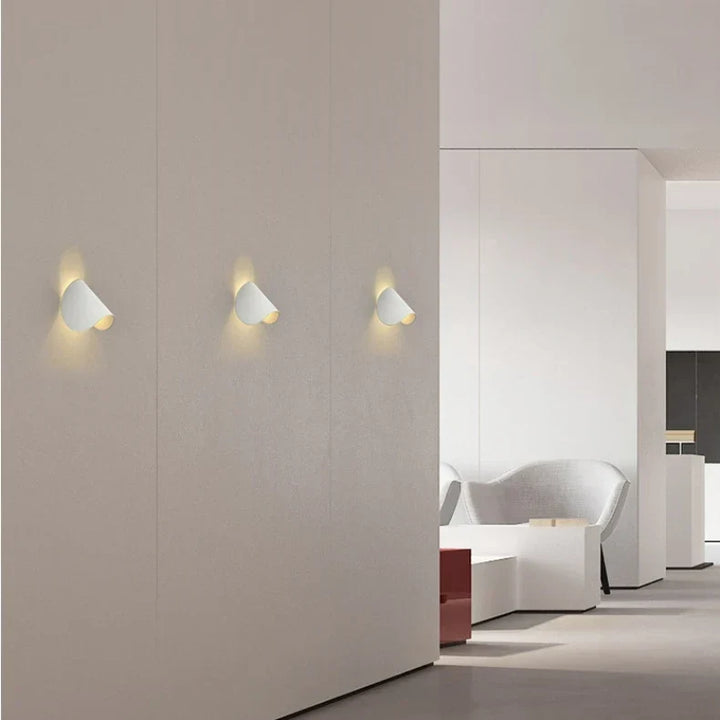 Trois appliques blanches alignées sur un mur beige dans un intérieur minimaliste, lumière douce diffusée vers le haut. 12