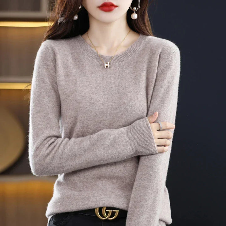 Pull col rond beige grisé porté avec un pantalon noir et une ceinture, bras croisé 16