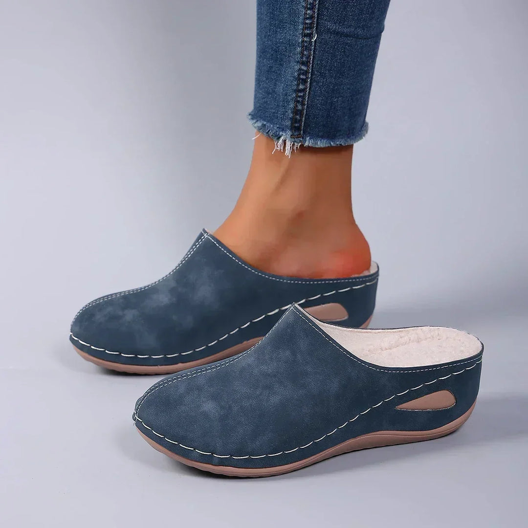 Chaussons bleus portés avec un jean, vue de trois quarts montrant la doublure polaire claire et la découpe de la semelle. 4