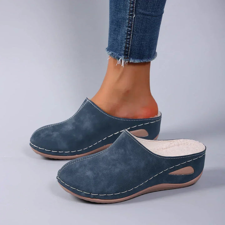 Chaussons bleus portés avec un jean, vue de trois quarts montrant la doublure polaire claire et la découpe de la semelle. 4