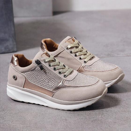Paire de baskets beige clair posée sur le sol, avec lacets dorés scintillants, zip latéral et empiècements brillants strassés. 2