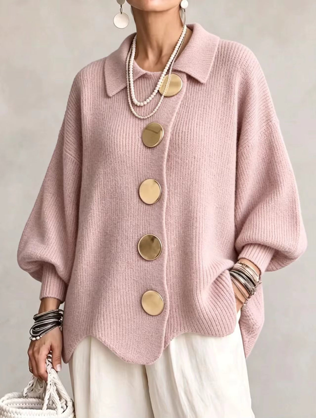 Vue de face du cardigan rose pâle en maille côtelée, grands boutons dorés et bas ondulé, porté avec un pantalon blanc. 6
