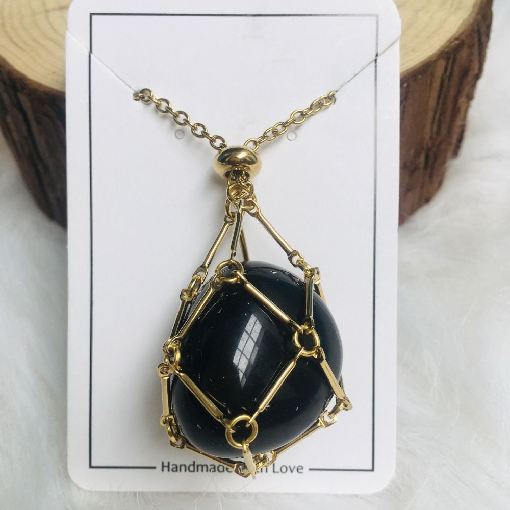 Collier doré dont le filet enserre une grosse pierre noire polie, présenté sur une carte blanche devant une rondelle de bois. 7