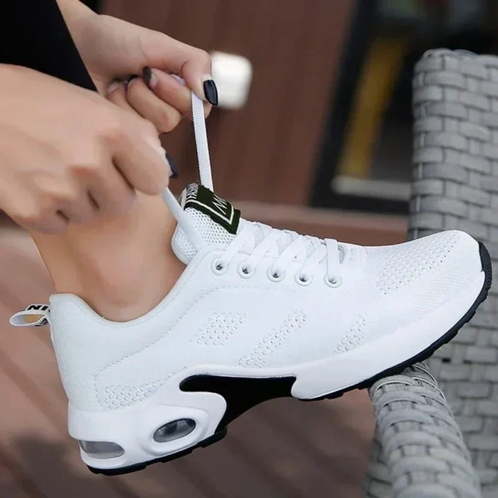 Baskets blanches en maille à semelle à coussin d'air, portées par une femme qui serre le lacet de sa chaussure. 1