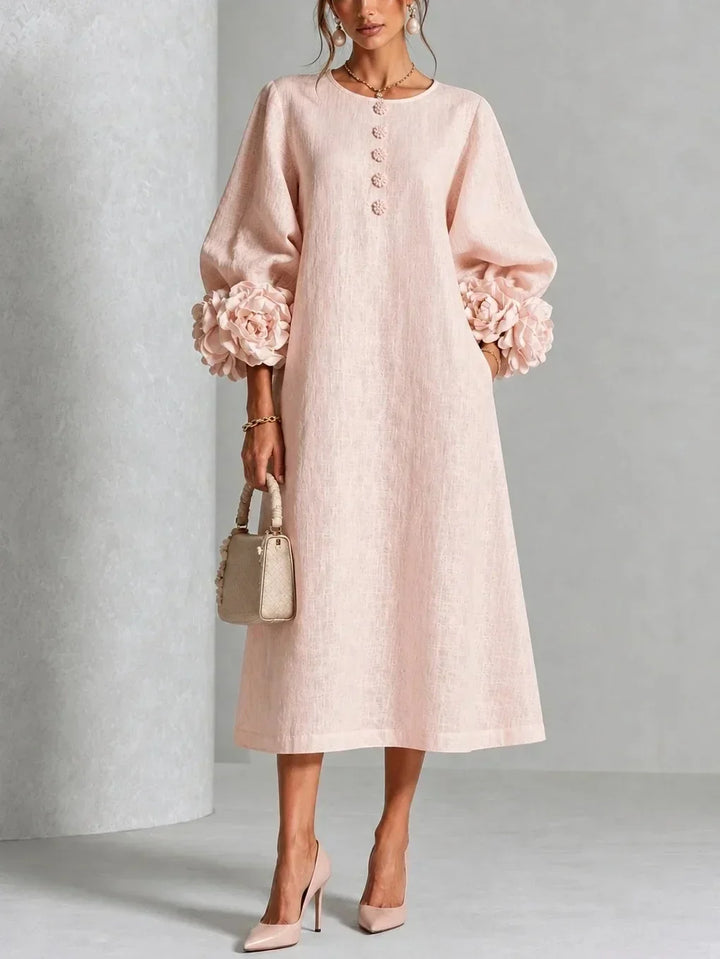 Version rose pâle de la robe portée de face, manches bouffantes à grosses fleurs, boutons fleuris, sac beige et escarpins roses. 4