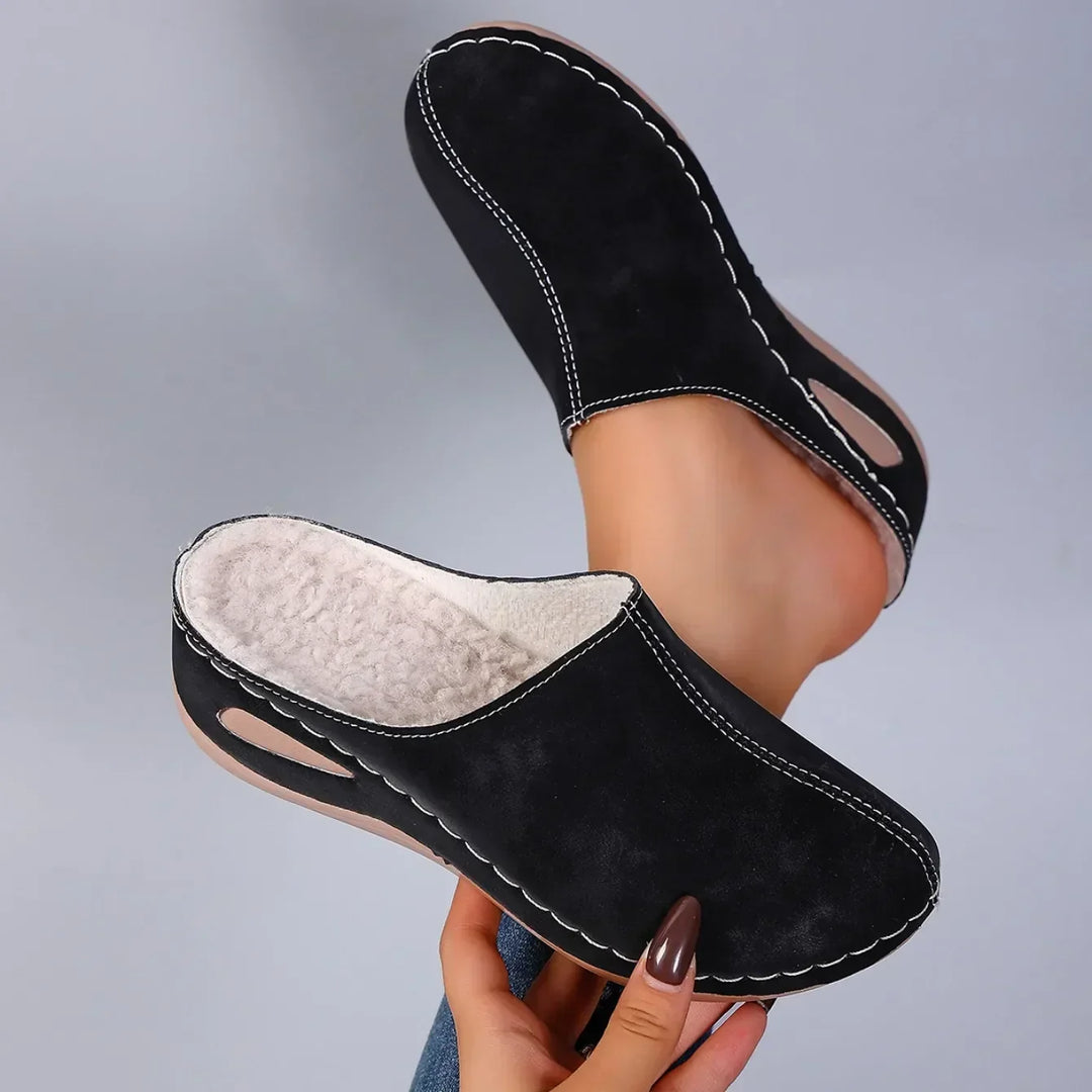 Paire de chaussons noirs tenue en main, l'un retourné pour montrer la doublure polaire épaisse, l'autre porté au pied. 5