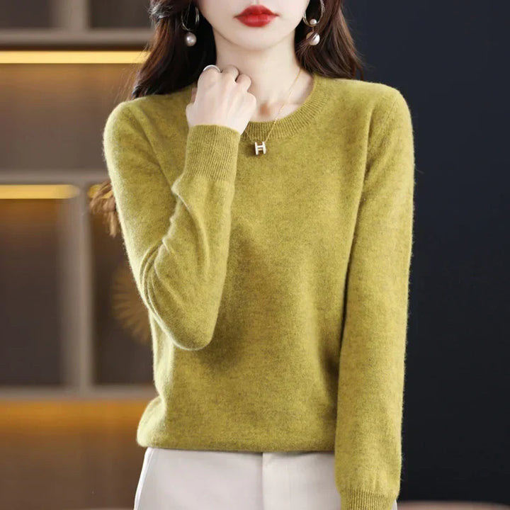 Pull col rond vert moutarde porté avec un pantalon crème, main relevée près du col 13