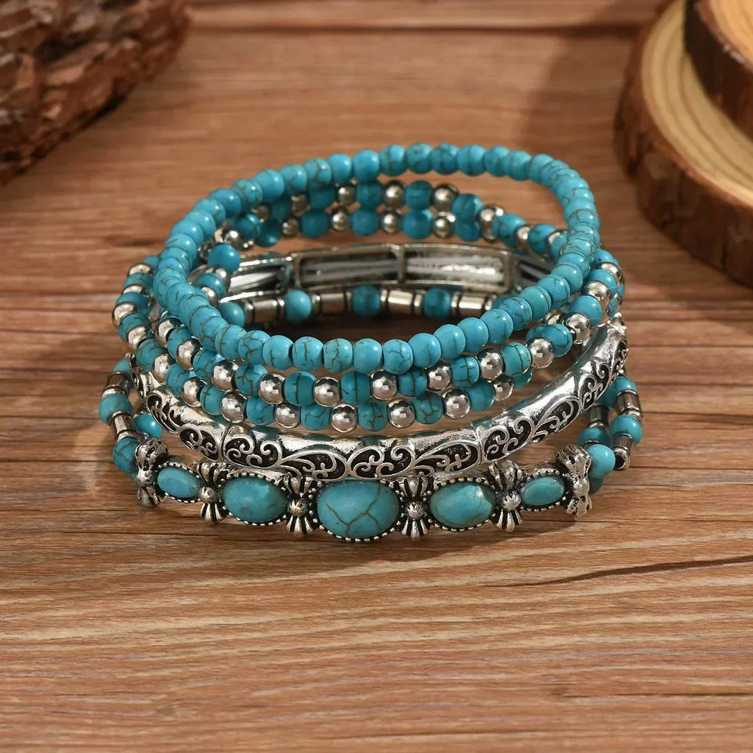 Les cinq bracelets empilés à plat sur une table en bois, détail des perles craquelées, de la tige ciselée et des pierres ovales. 3