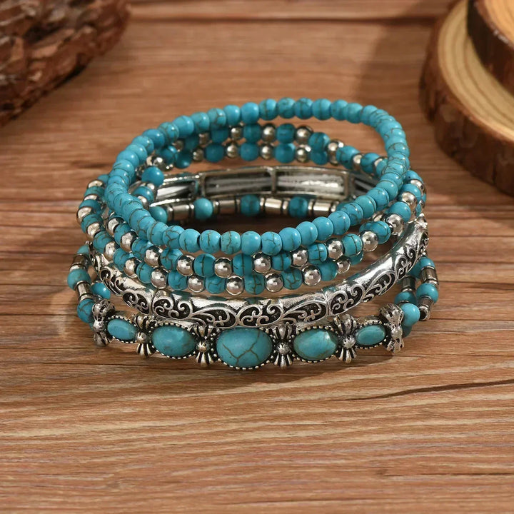 Les cinq bracelets empilés à plat sur une table en bois, détail des perles craquelées, de la tige ciselée et des pierres ovales. 3