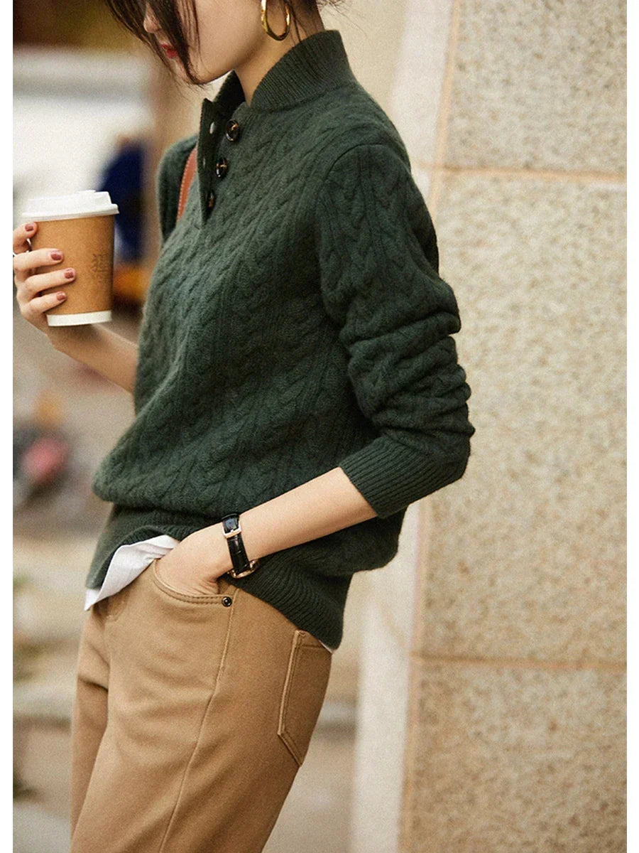 Femme de profil tenant un gobelet, pull vert foncé torsadé à col boutonné, pantalon marron clair, chemise blanche dépassant. 8