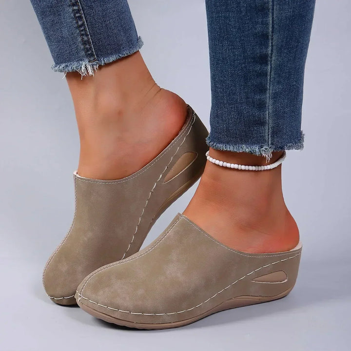 Chaussons beiges portés avec un jean effiloché et une chaîne de cheville de perles blanches, vue de côté sur la semelle. 3
