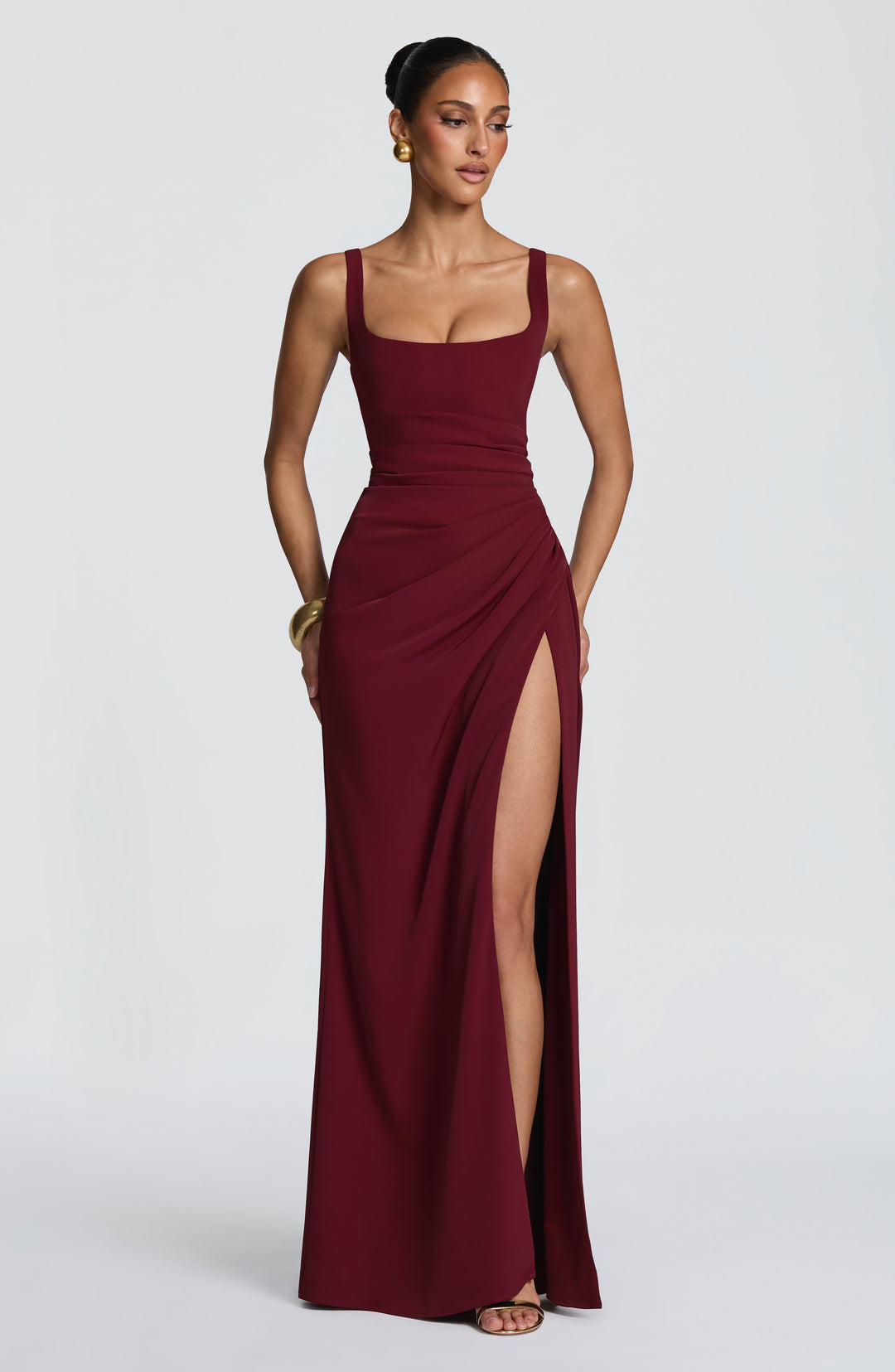 Robe longue bordeaux portée de face, encolure carrée, taille drapée et fente haute, avec bijoux dorés. 17