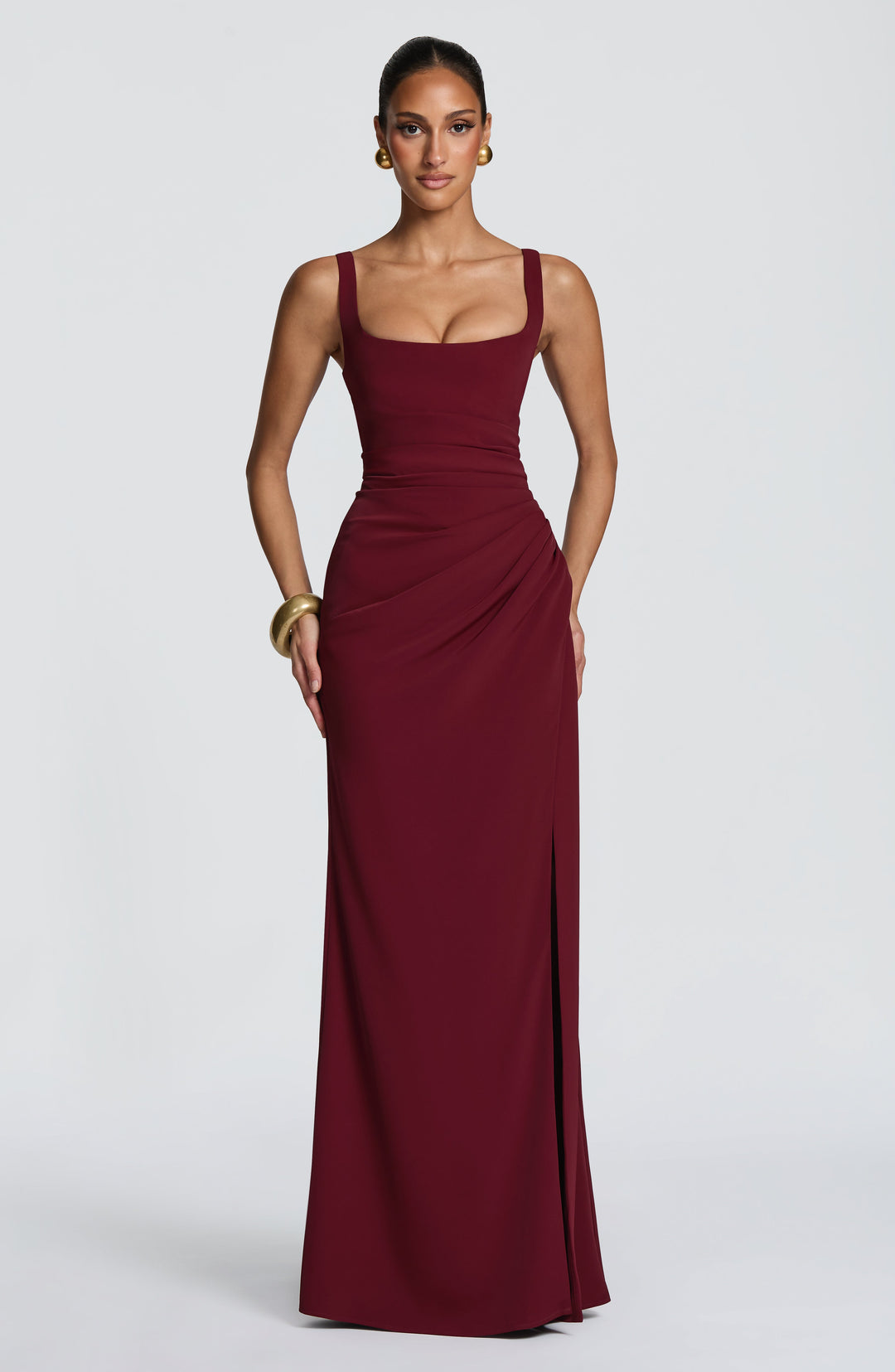 Robe bordeaux portée de face, bras le long du corps, drapé sur la hanche et fente latérale, bracelet doré. 20
