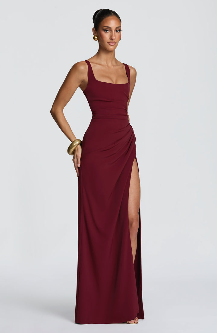 Robe bordeaux de trois quarts, une main sur la hanche, mettant en valeur le drapé et la fente haute. 19