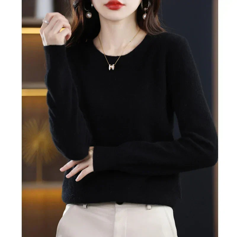 Pull col rond noir porté avec un pantalon crème, une main levée et l'autre sur le ventre 19