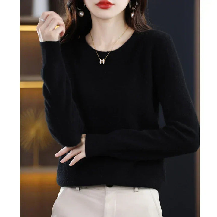 Pull col rond noir porté avec un pantalon crème, une main levée et l'autre sur le ventre 19