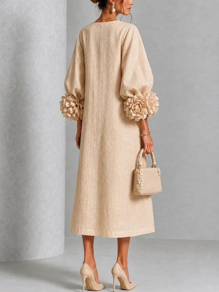 Robe beige vue de dos, dos uni et droit, manches bouffantes terminées par de grosses fleurs en relief, sac beige tenu à la main. 7