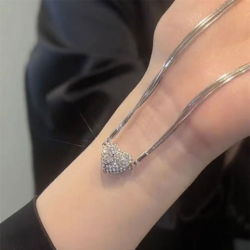 Le collier tendu sur un poignet, montrant les chaînes argentées fines et le cœur en strass formé de deux moitiés magnétiques jointes. 7