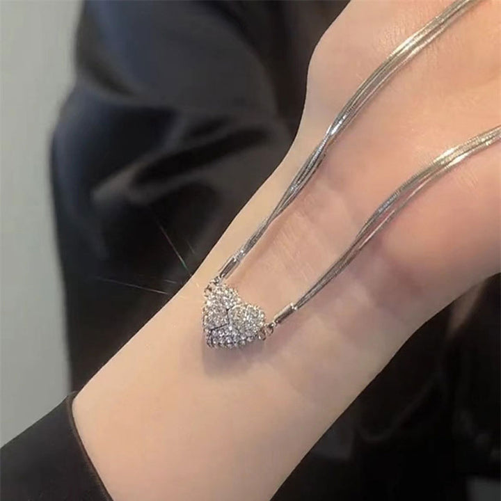 Le collier tendu sur un poignet, montrant les chaînes argentées fines et le cœur en strass formé de deux moitiés magnétiques jointes. 7