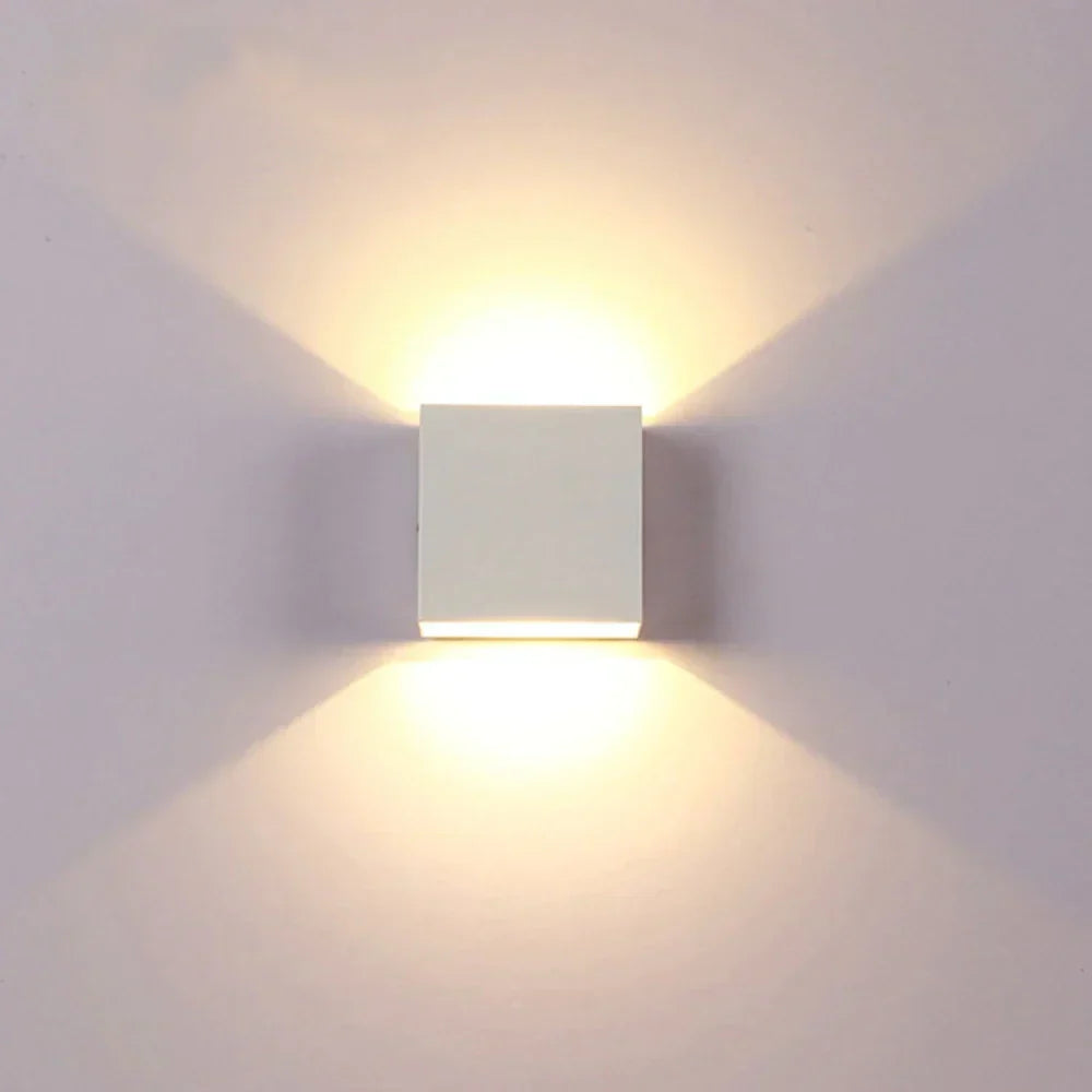 Applique cubique blanche allumée vue de face sur un mur clair, avec une lumière chaude projetée vers le haut et le bas. 17