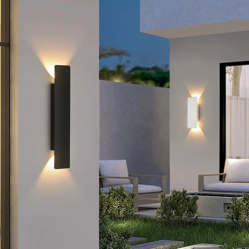 Applique noire en gros plan sur un mur de terrasse, une seconde applique blanche visible au fond près d'un salon de jardin. 5