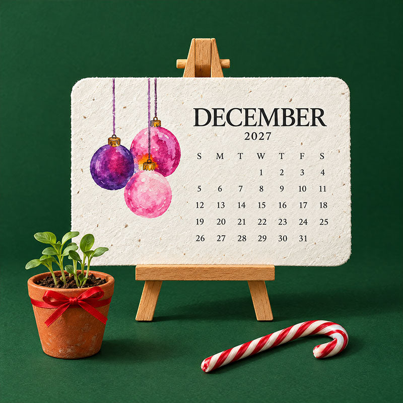 Page de décembre ornée de boules roses et violettes, posée sur chevalet près d'un pot de jeunes pousses 3