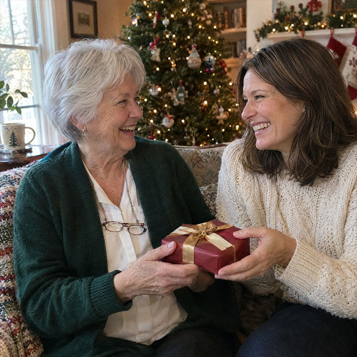 Deux femmes souriantes devant un sapin illuminé s'offrent un petit cadeau emballé de rouge et de ruban doré 4