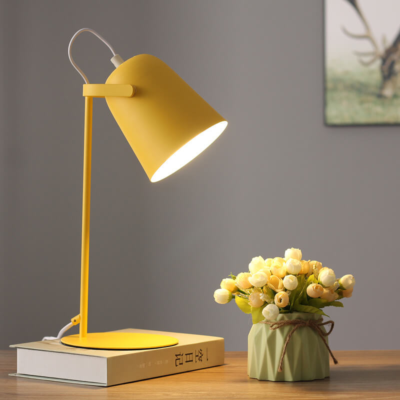 Lampe jaune allumée sur un livre près d'un vase vert avec fleurs, devant un mur gris. 7