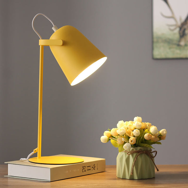 Lampe jaune allumée sur un livre près d'un vase vert avec fleurs, devant un mur gris. 7