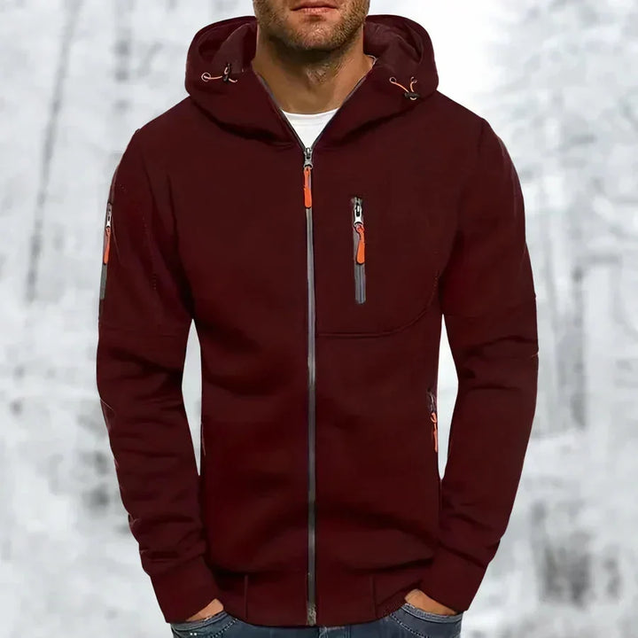 Sweat à capuche zippé bordeaux porté par un modèle, avec zips orange et poche poitrine zippée, fond enneigé. 4