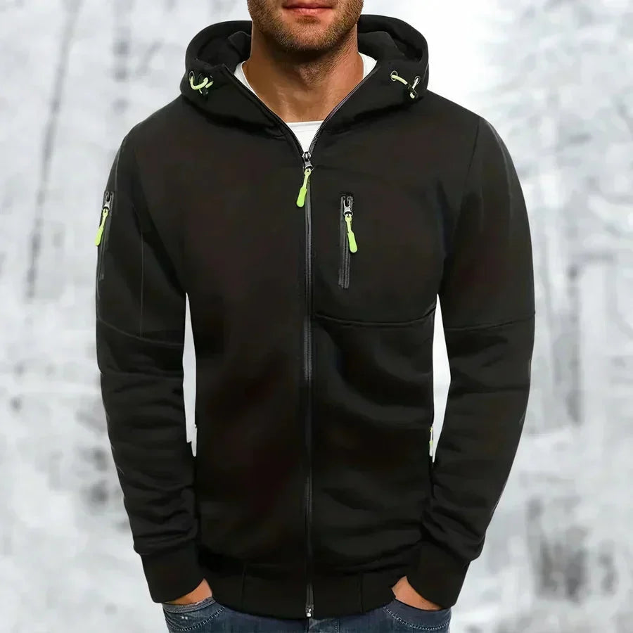 Sweat à capuche zippé noir porté de face par un modèle, zips vert citron contrastés, fond de forêt enneigée. 7