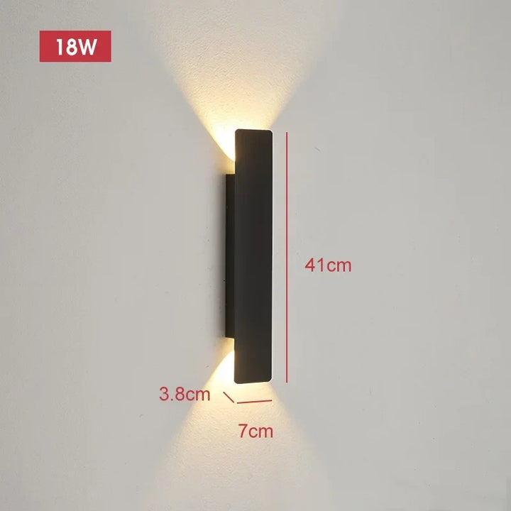 Applique noire de 41 cm de haut, 7 cm de large et 3,8 cm de profondeur, allumée sur un mur clair avec ses cotes. 11