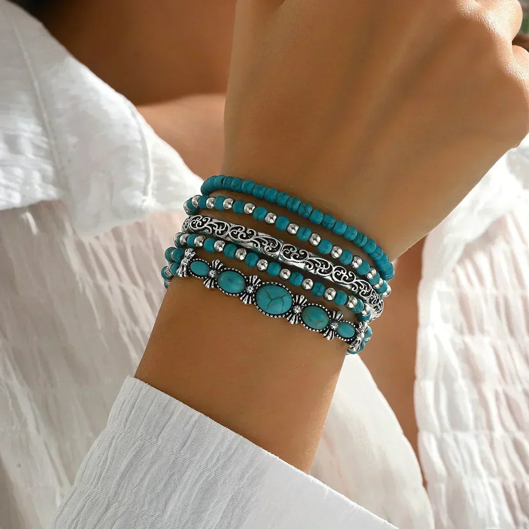 Cinq bracelets superposés portés au poignet, vus de l'autre côté, avec une chemise blanche et le bracelet à pierres ovales en bas. 2