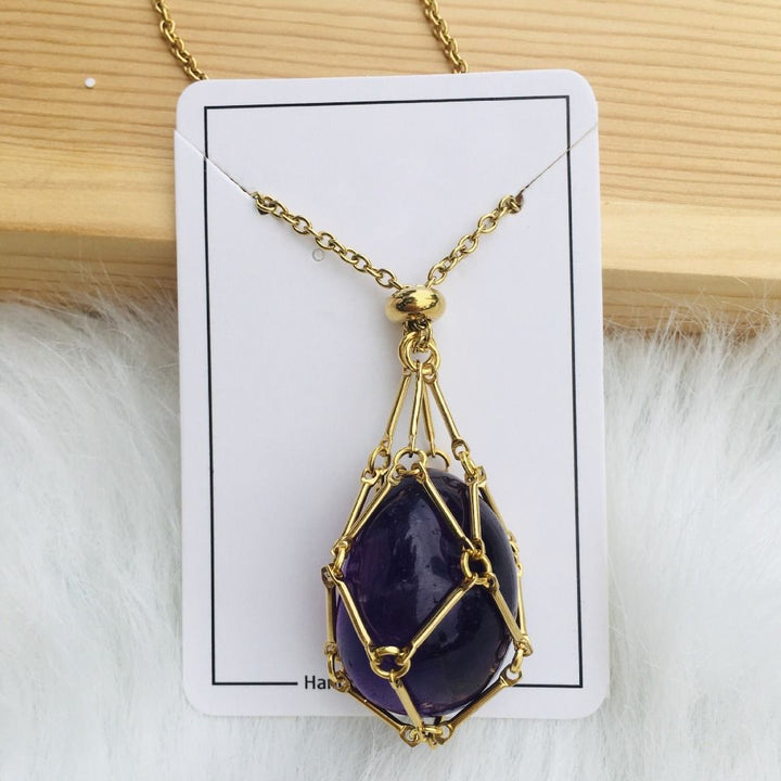 Collier doré avec filet de maillons retenant une pierre violet foncé ovale, sur une carte blanche contre du bois. 16