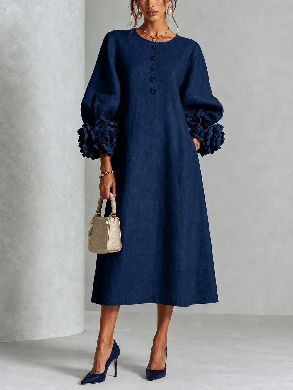 Version bleu marine de la robe portée de face, avec grosses fleurs aux poignets, boutons fleuris, sac beige et escarpins assortis. 2