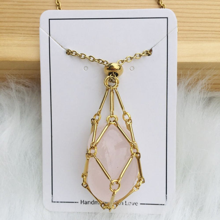 Collier doré avec filet entourant une pierre rose pâle allongée, présenté sur une carte blanche avec fourrure blanche en dessous. 10