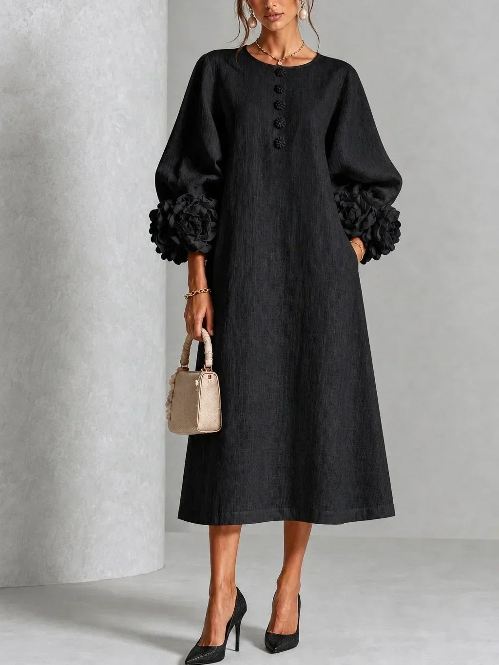 Version noire de la robe portée de face, manches bouffantes à fleurs en relief, boutons fleuris, sac beige et escarpins noirs. 5