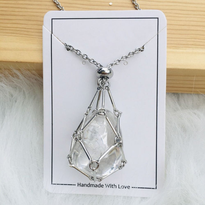 Collier argenté avec filet autour d'une pierre de cristal transparent en goutte, présenté sur une carte blanche posée sur du bois. 15