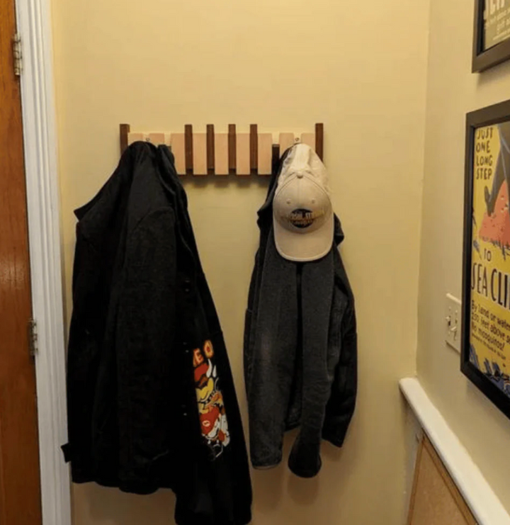 Porte-manteau en bois clair installé dans un couloir jaune, avec deux vestes sombres et une casquette accrochées. 6