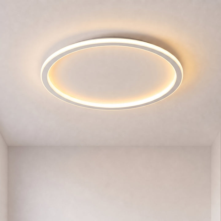 Plafonnier annulaire blanc allumé, lumière chaude, vu de face au plafond d'une pièce vide aux murs clairs. 1