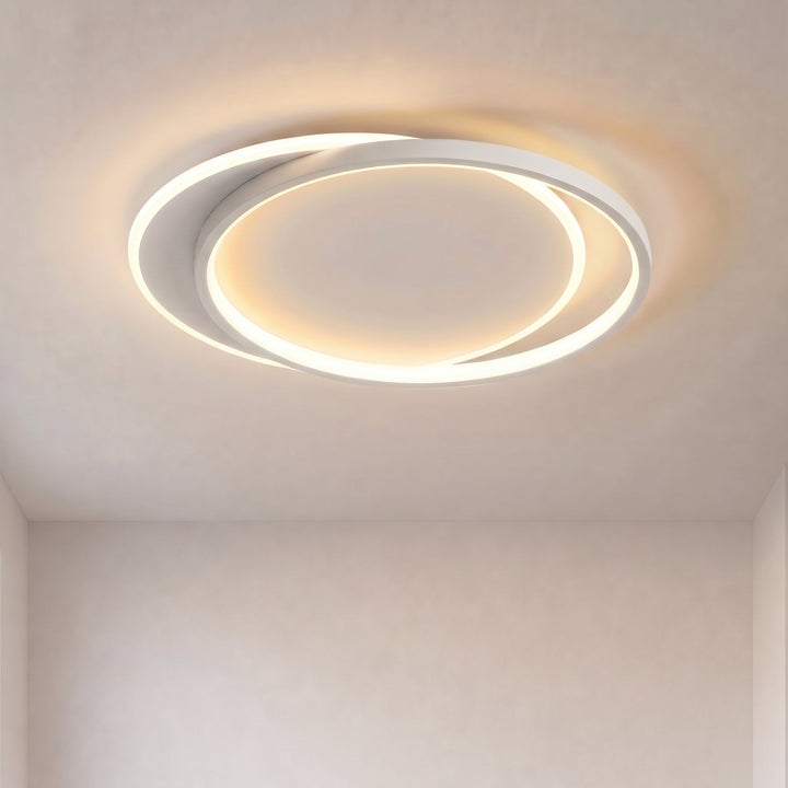 Plafonnier à deux anneaux blancs entrecroisés allumé, vu de dessous sur un plafond clair, lumière chaude 1