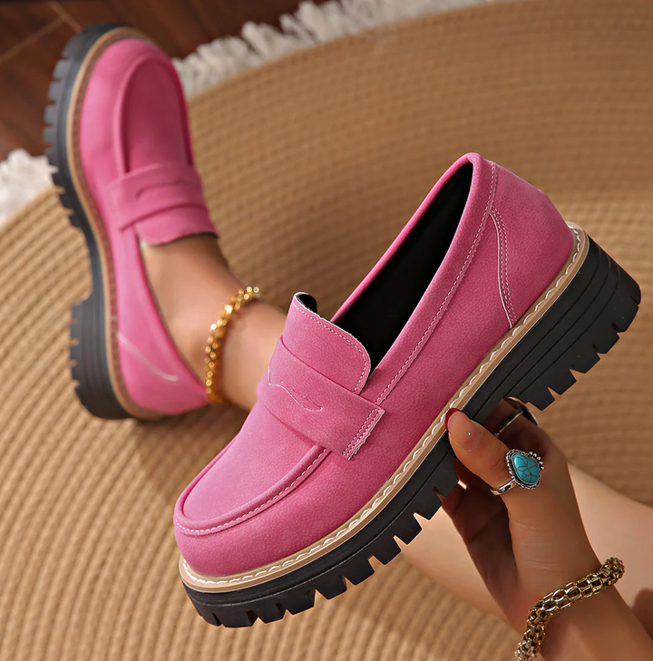 Mocassins roses fuchsia en daim, l'un tenu à la main au-dessus d'un tapis tressé, vue plongeante sur la plateforme crantée. 18