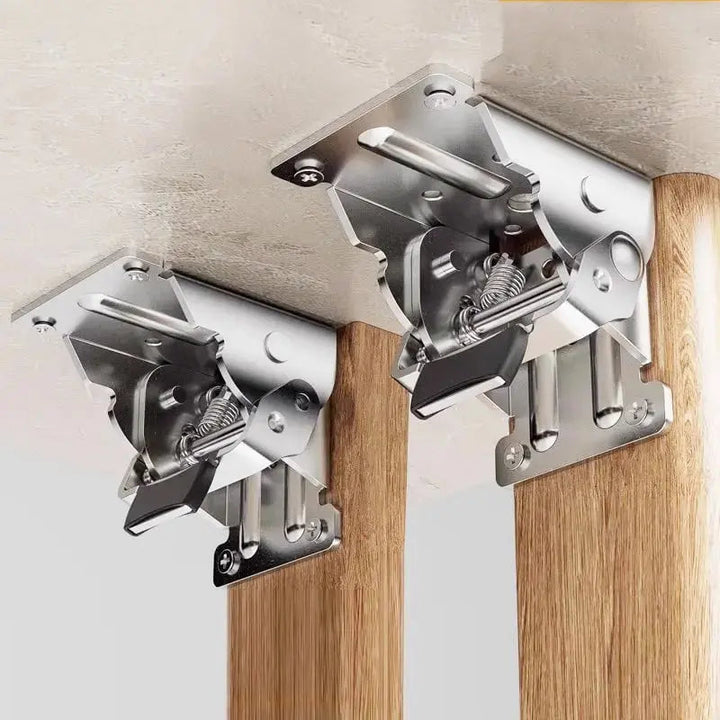 Deux supports pliants en métal argenté fixés sous un plateau, reliant chacun un pied en bois, vus de près avec leurs ressorts. 1