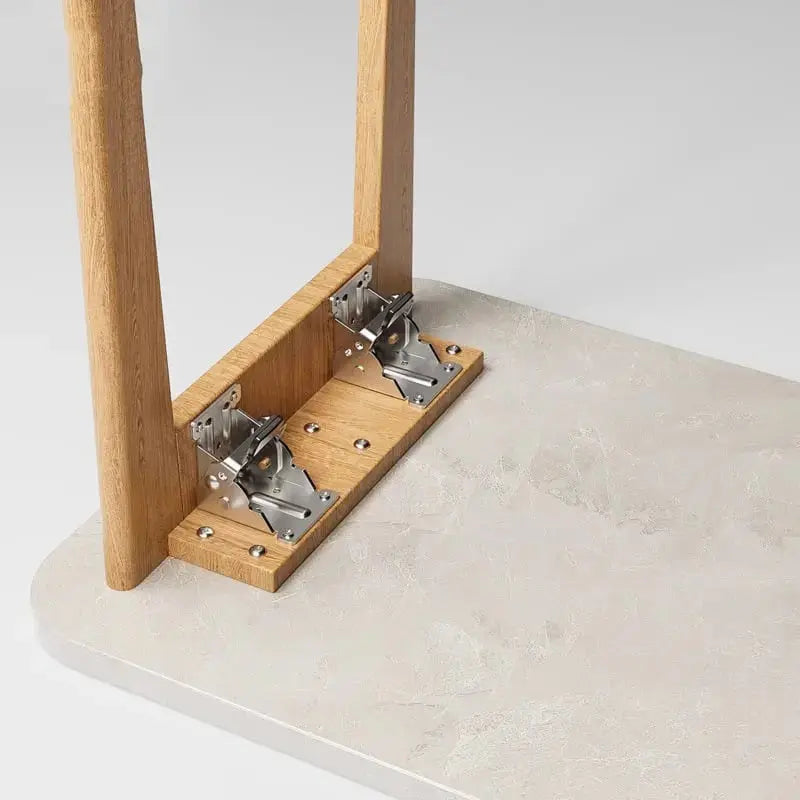 Deux supports pliants vissés sur une traverse en bois, pied replié contre le dessous d'un plateau de table clair. 2