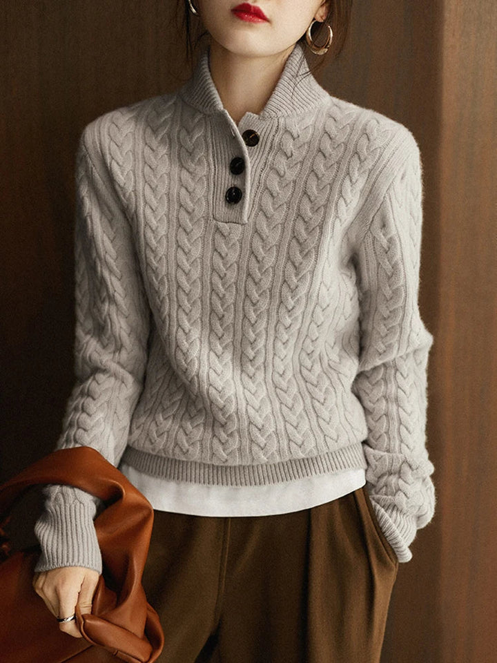 Pull gris torsadé à col montant et trois boutons, porté sur une chemise blanche avec pantalon marron, sac en cuir au bras. 14