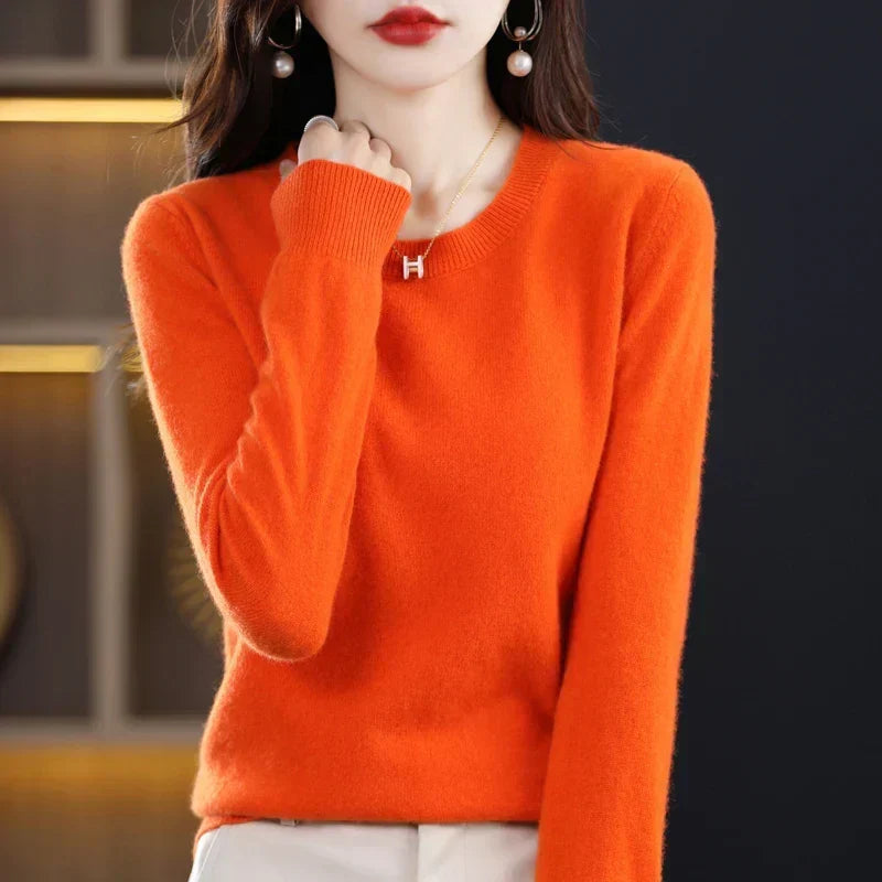 Pull col rond orange vif porté par une femme, main relevée vers le col, pantalon clair 14