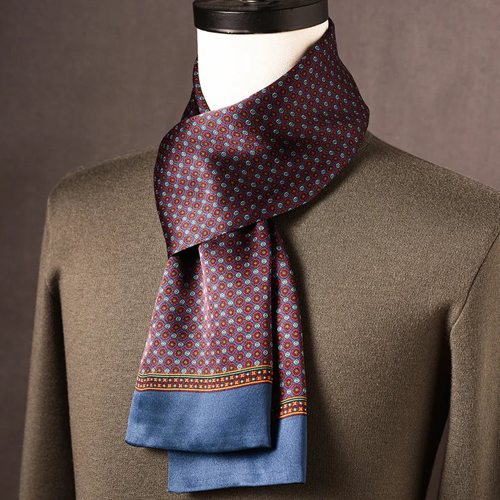 Foulard en soie bordeaux et bleu à petits motifs ronds, bordure bleue, noué autour du cou d'un mannequin sur pull kaki. 1