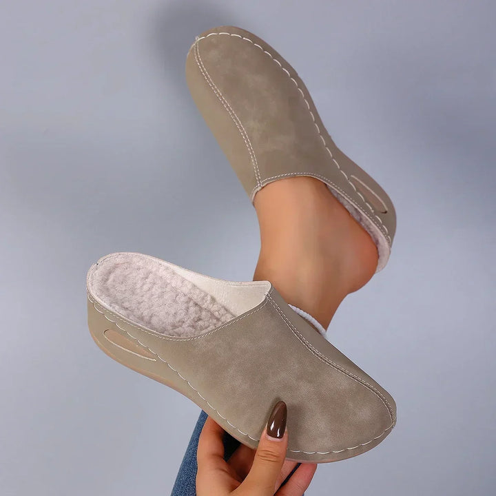 Paire de chaussons beige taupe tenue en main, intérieur en polaire douce visible, coutures claires et semelle compensée évidée. 6