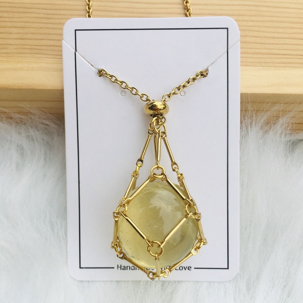 Collier doré avec filet de maillons enserrant une pierre jaune pâle arrondie, présenté sur une carte blanche posée sur du bois. 1